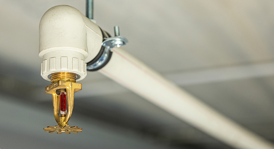 Close up image of fire sprinkler with fire in background. Fire sprinklers are part of an integrated water piping system designed for life and fire safety.